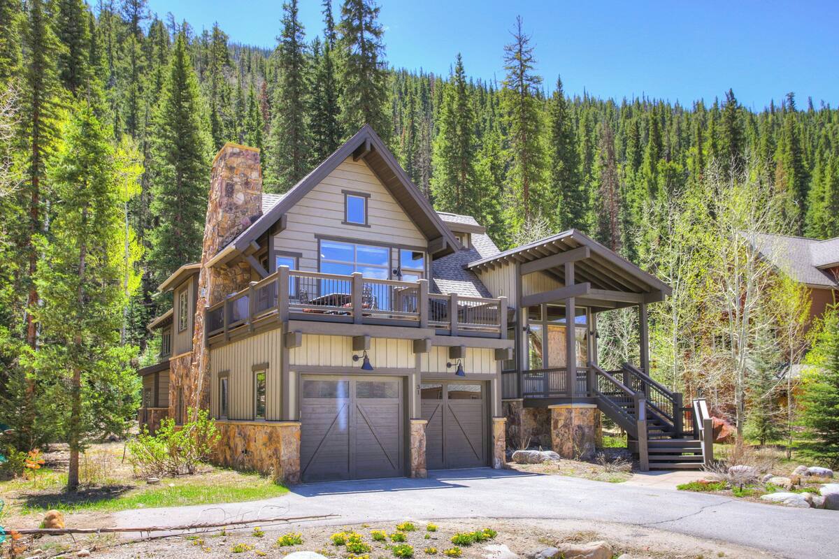 A two-story lodge with a stone facade, a balcony, and a staircase leading to a second-floor deck.