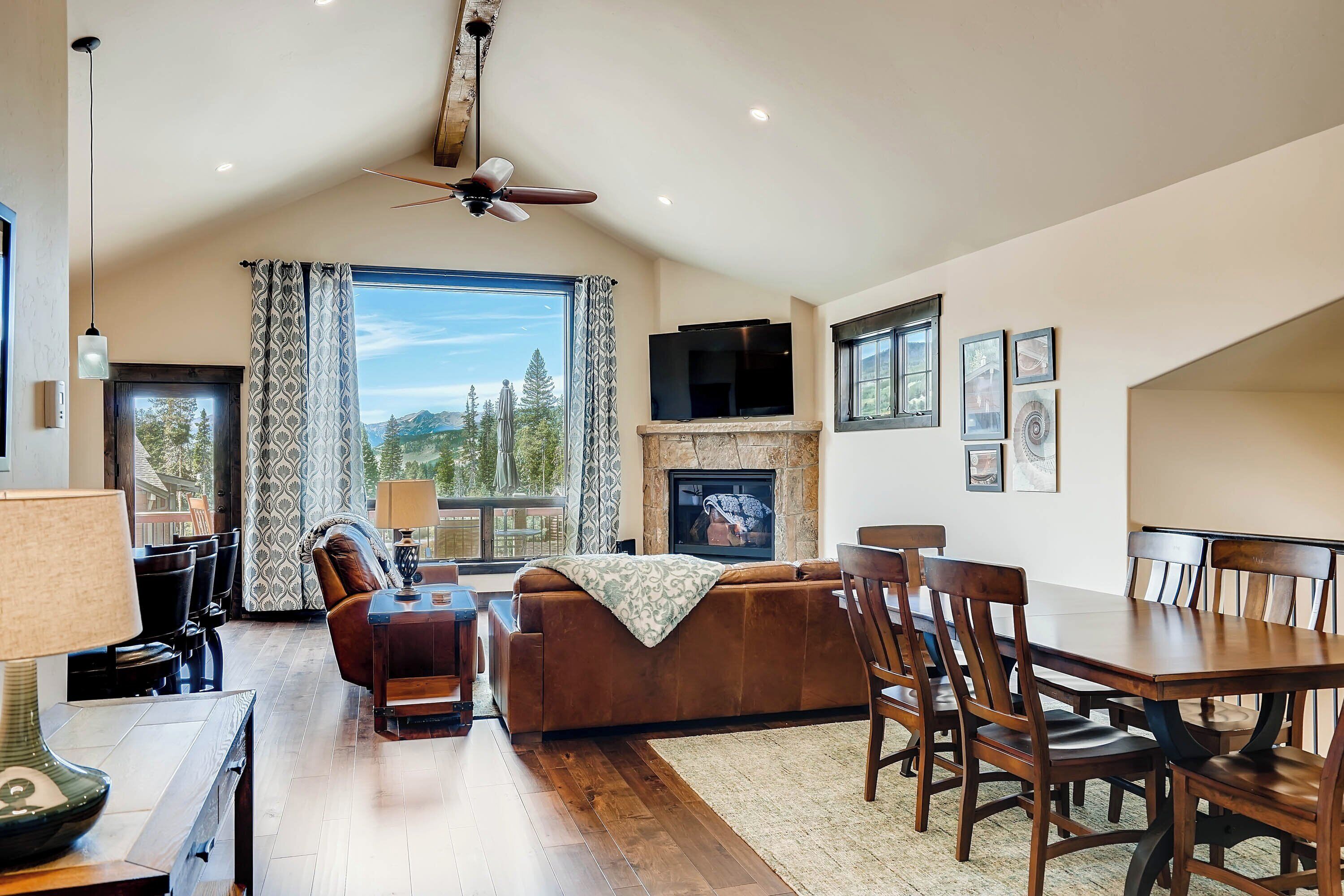 A spacious living room with a fireplace, a dining area, and a large window offering a view of the outdoors.