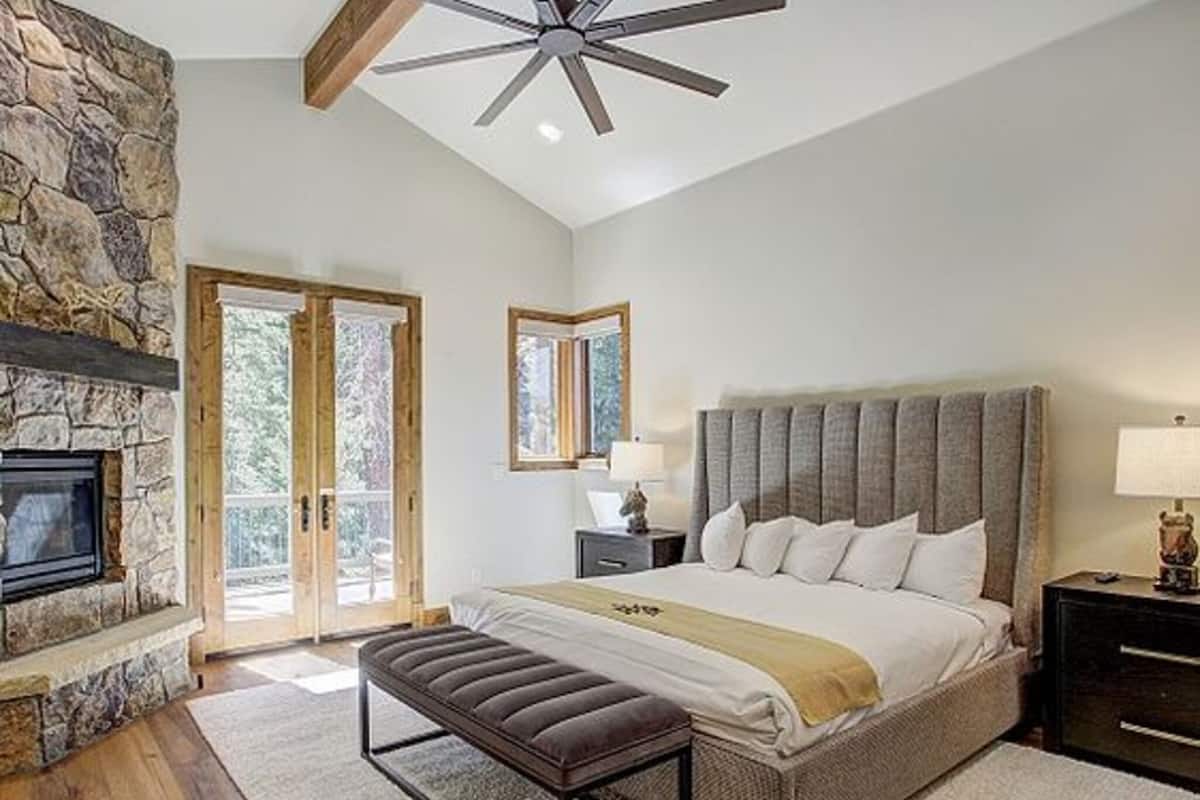 A bedroom with a stone fireplace, a large bed with a headboard, a bench, and a ceiling fan.