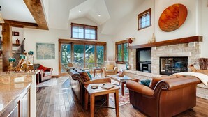 A spacious living room with a fireplace, wooden floors, and large windows offering a view of the outdoors. - Keystone Private Homes by Vail Resorts (Keystone)