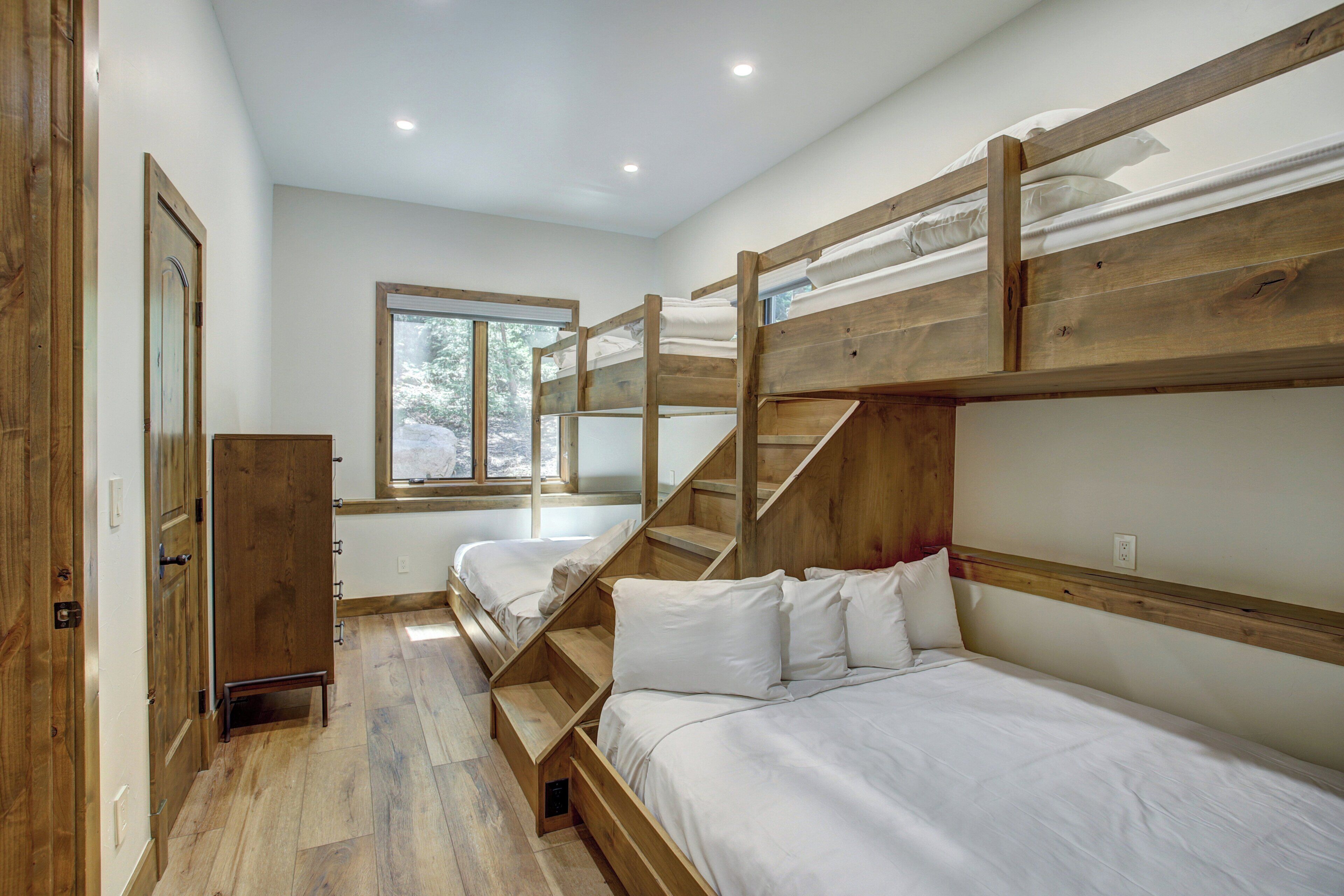 A bunk bed room with wooden headboards, a window, and a staircase.