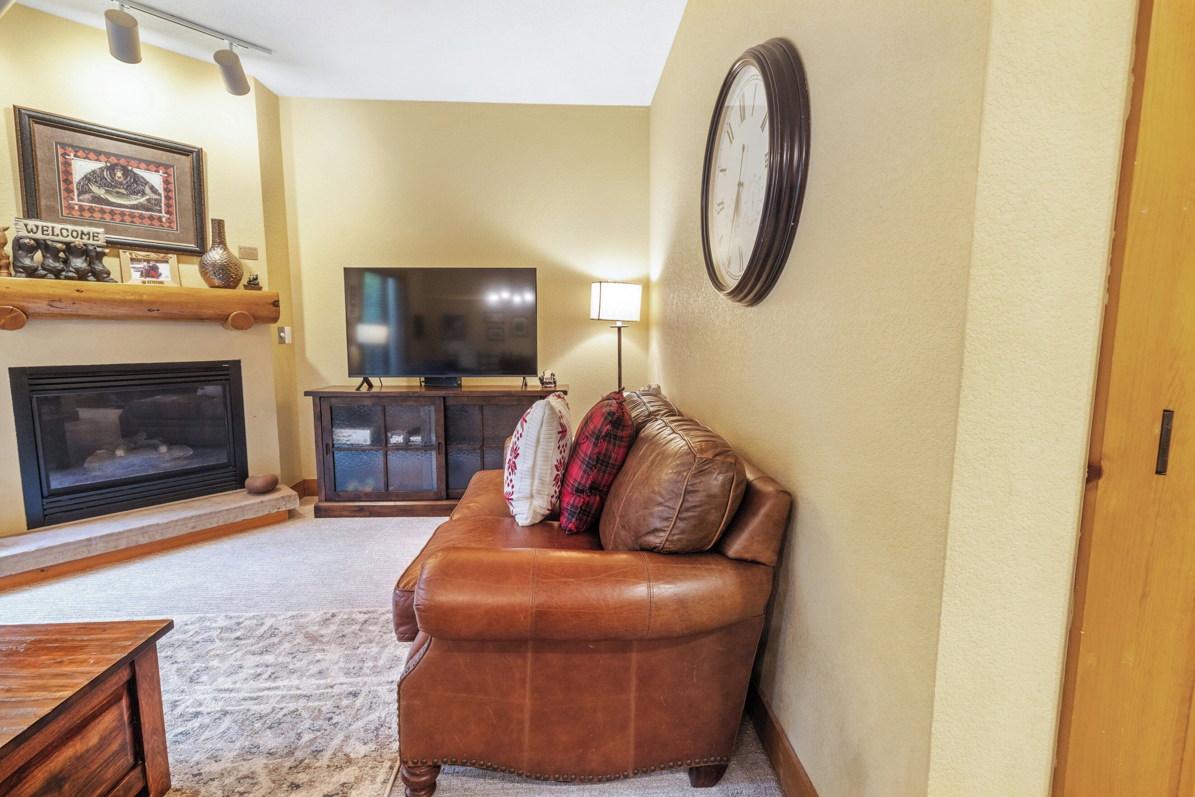 A living room with a fireplace, a television, a clock, and a sofa with decorative pillows.