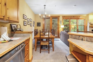 A kitchen with wooden cabinets, a dining table, and chairs. There is a chandelier, a window with blinds, and a sofa in the living area. - East Keystone by Vail Resorts (Keystone)