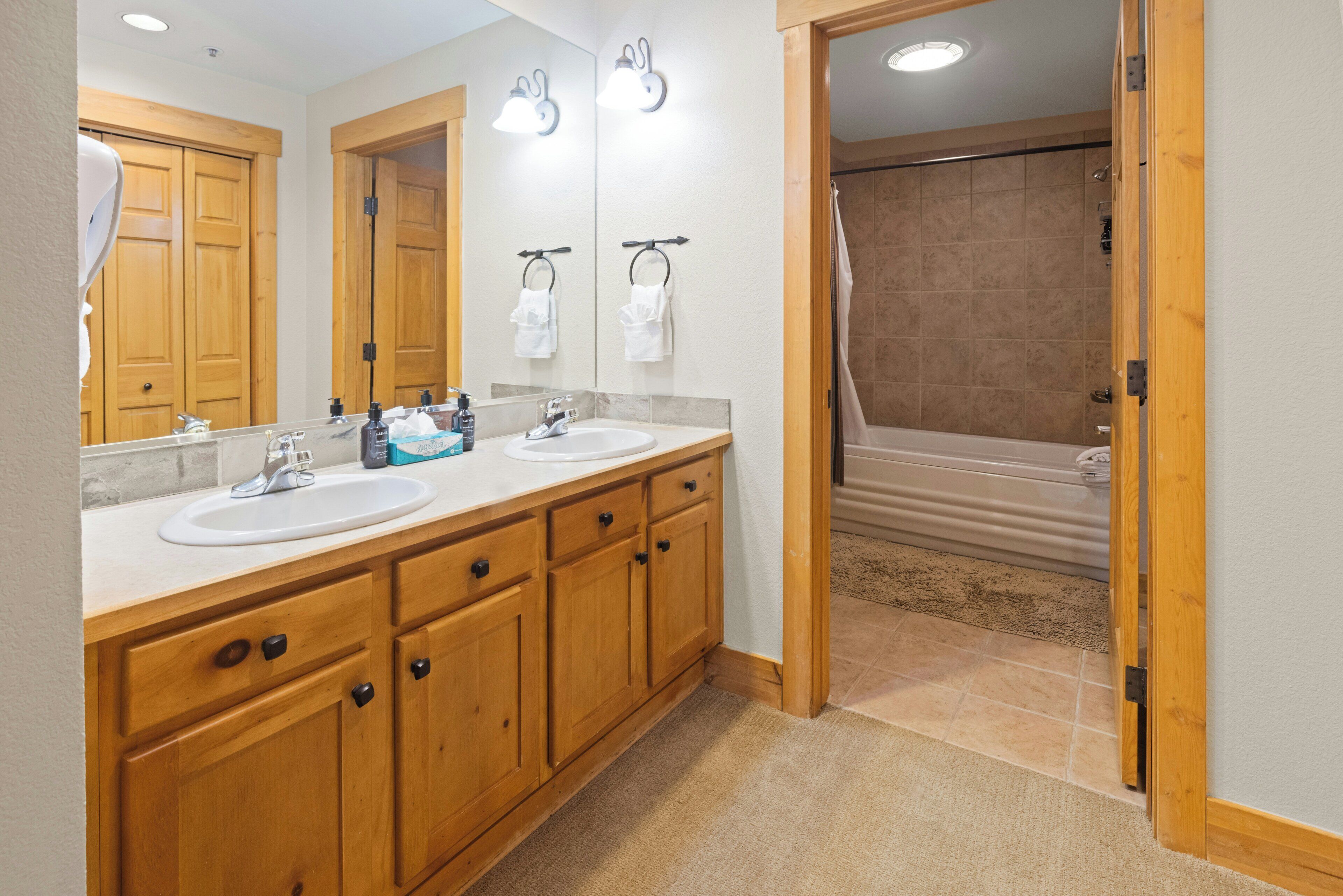 Un baño con armarios de madera, lavabo doble y un espejo grande.
