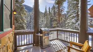 A wooden deck with a barbecue grill, benches, and a view of snow-covered trees and mountains. - East Keystone by Vail Resorts (Keystone)