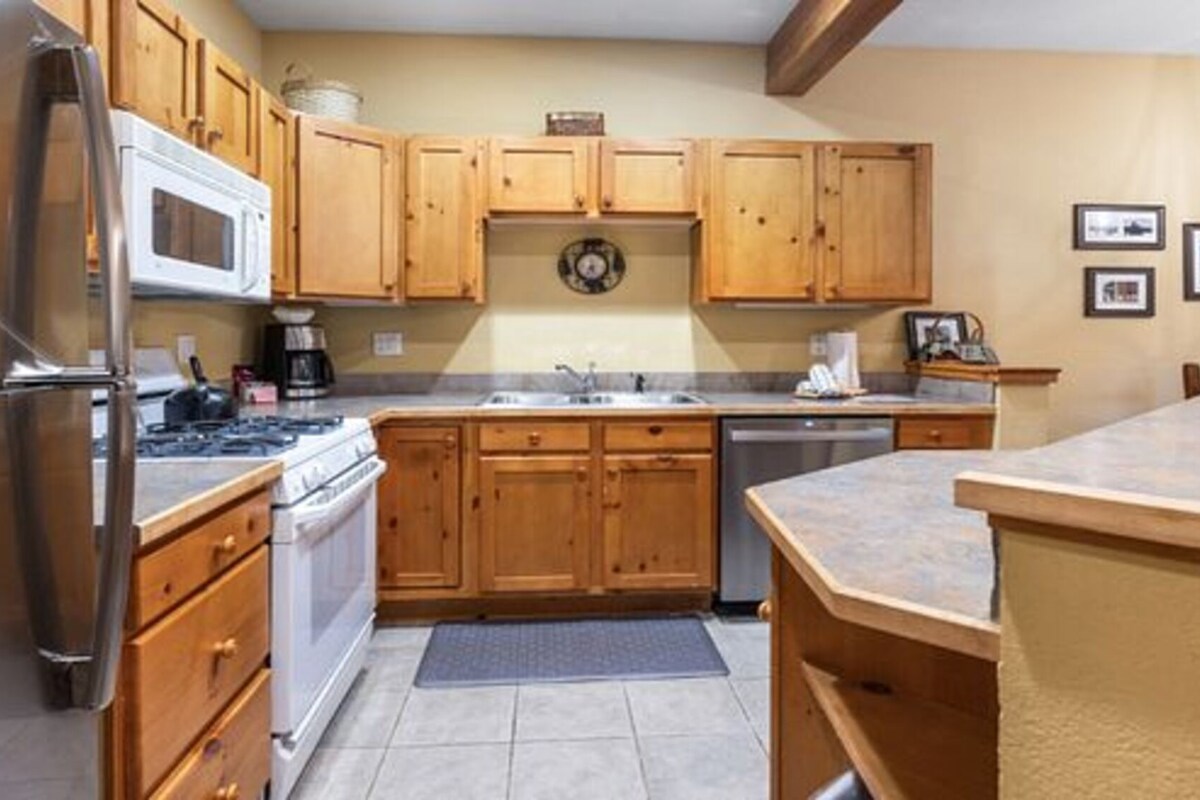 A kitchen with wooden cabinets, stainless steel appliances, and a tiled floor.