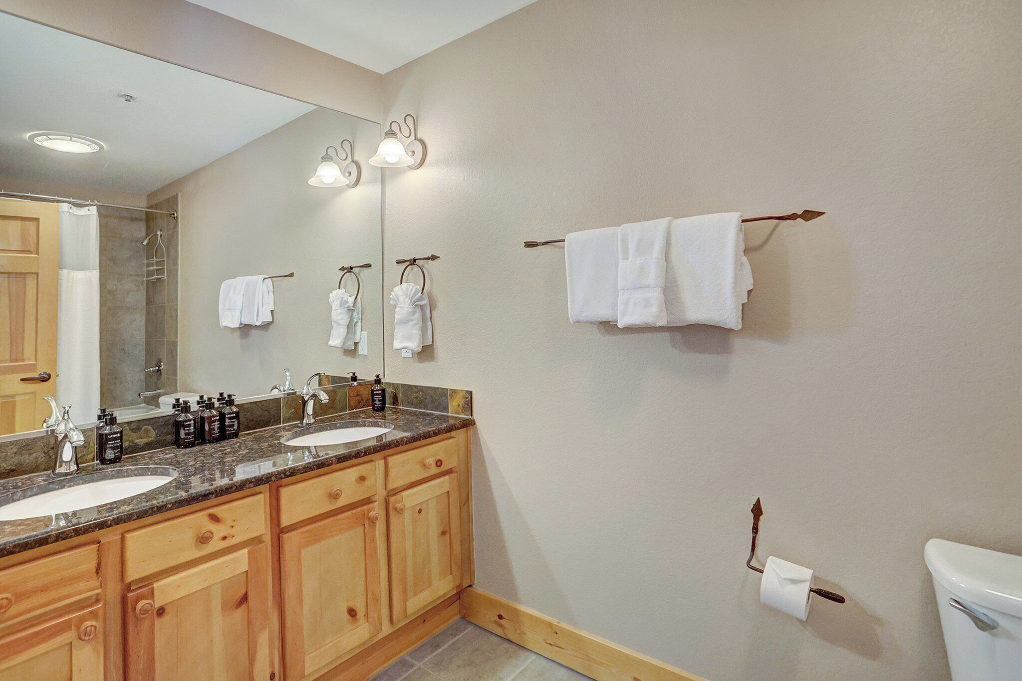 A bathroom with a double sink vanity, wooden cabinets, a large mirror, and a towel rack.