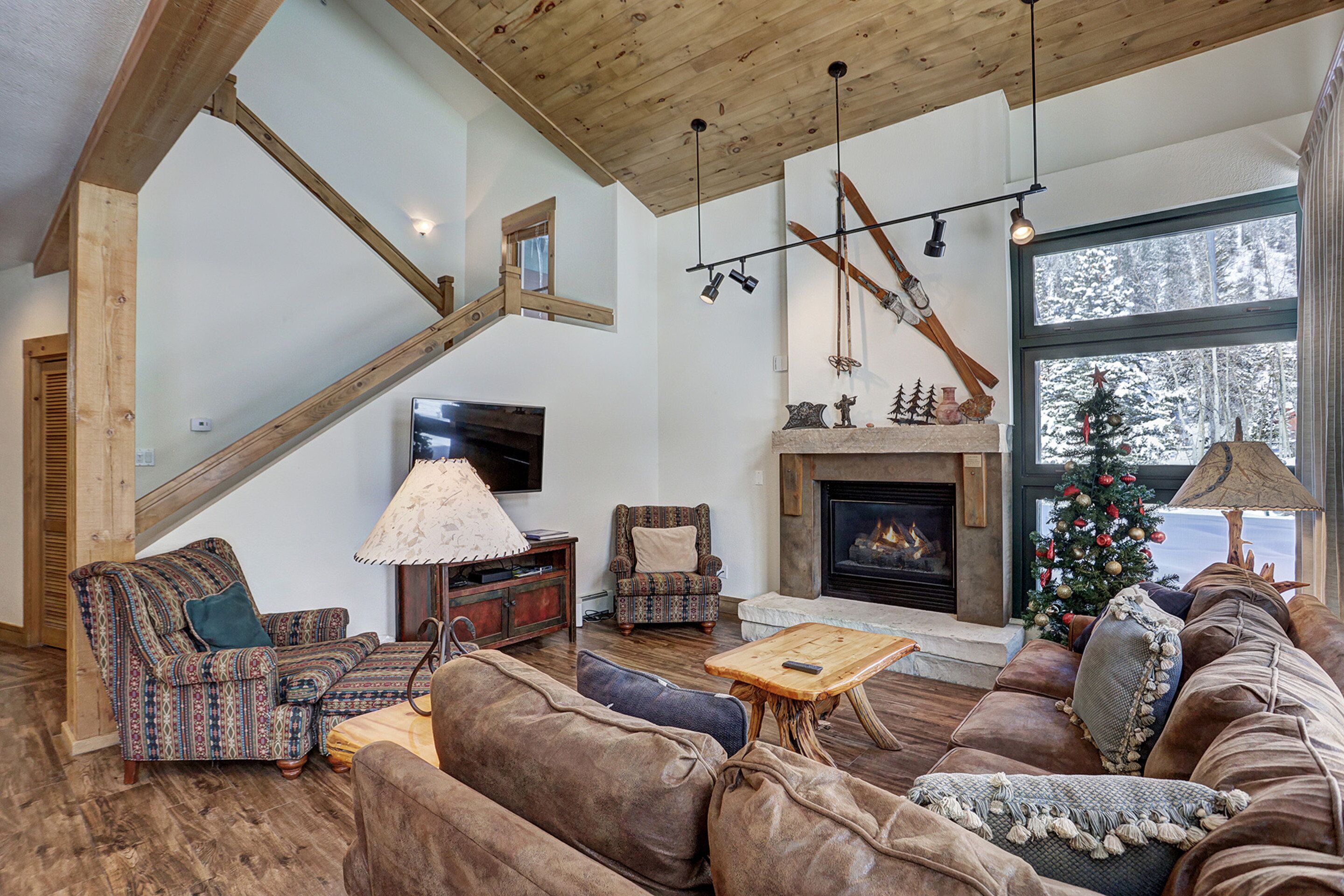 A cozy living room with a fireplace, a staircase, and a large window with a view of a snowy landscape.