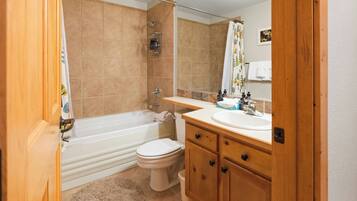 Un baño con bañera, inodoro y tocador con espejo.