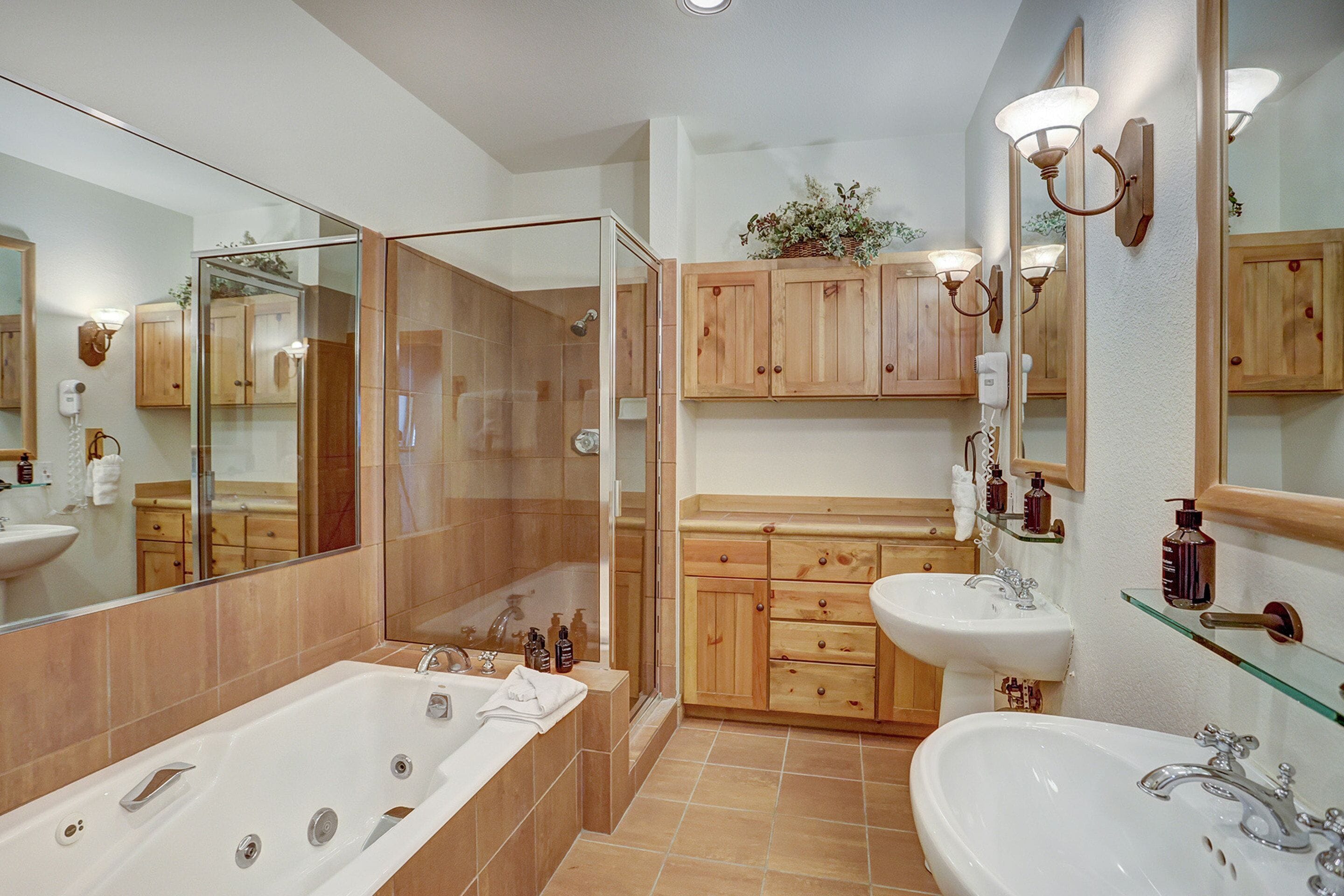 A modern bathroom with a glass-enclosed shower, wooden cabinets, a large bathtub, and two sinks.