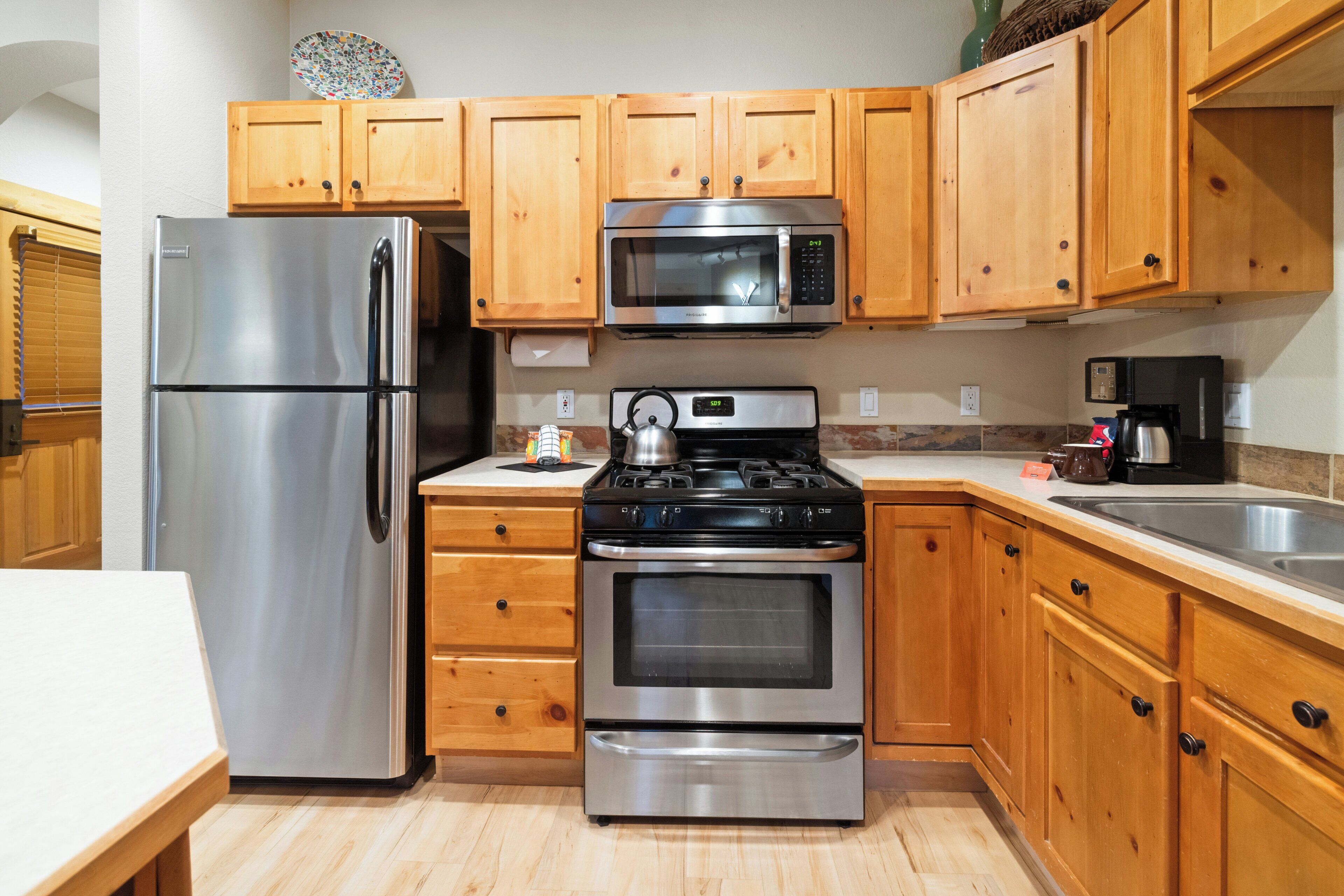A modern kitchen with wooden cabinets, stainless steel appliances including a refrigerator, microwave, stove, and oven.