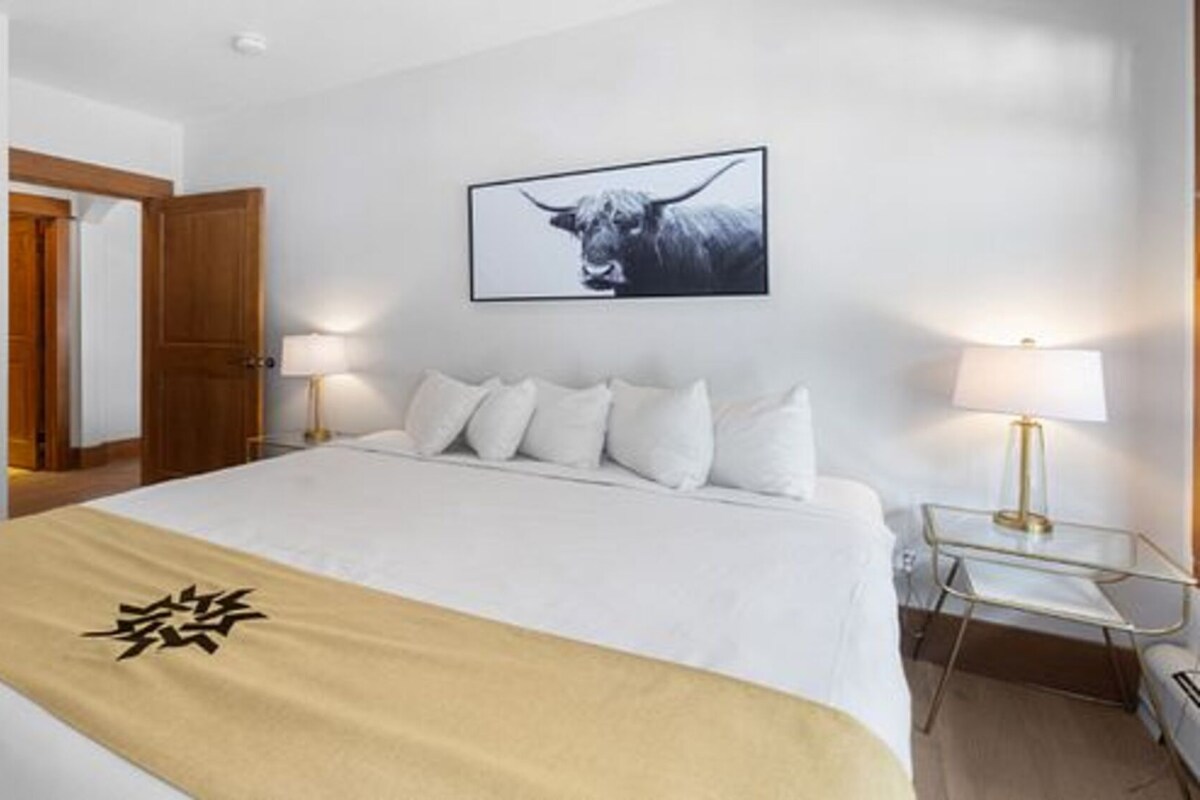 A hotel room with a bed, a bedside lamp, a framed picture on the wall, and a door.