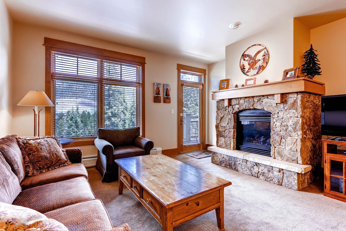 A living room with a stone fireplace, a sofa, a coffee table, and a television.
