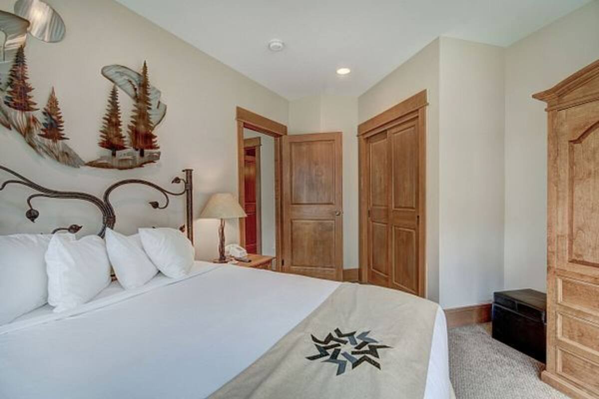 A bedroom with a bed, wooden wardrobe, and a wall-mounted artwork.