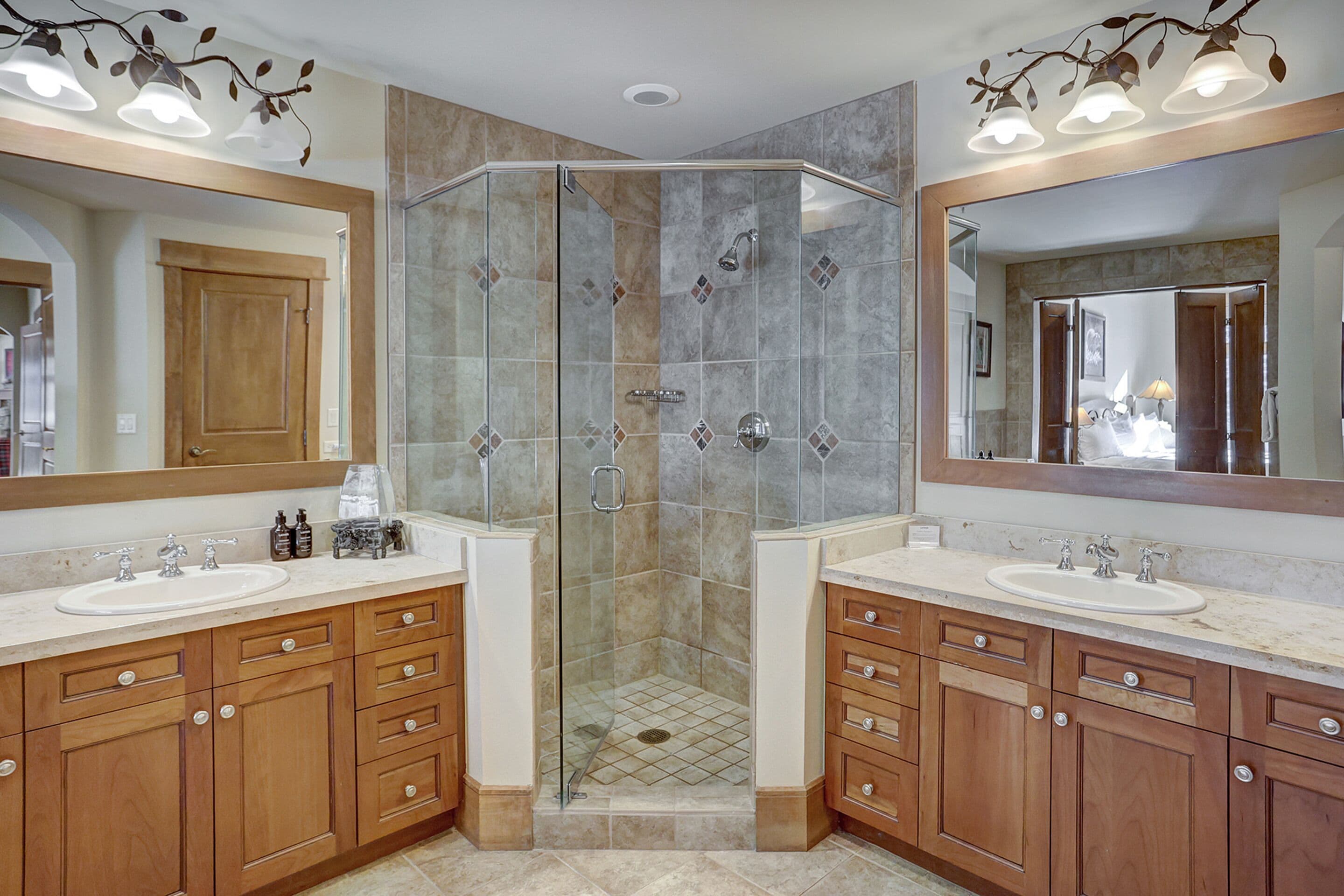 A modern bathroom with two sinks, wooden cabinets, and a glass-enclosed shower.