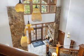 A stone-floored interior with hanging lamps, a wooden bench, and a staircase.