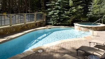 Une piscine bordée de pierres, un jacuzzi et des chaises longues.