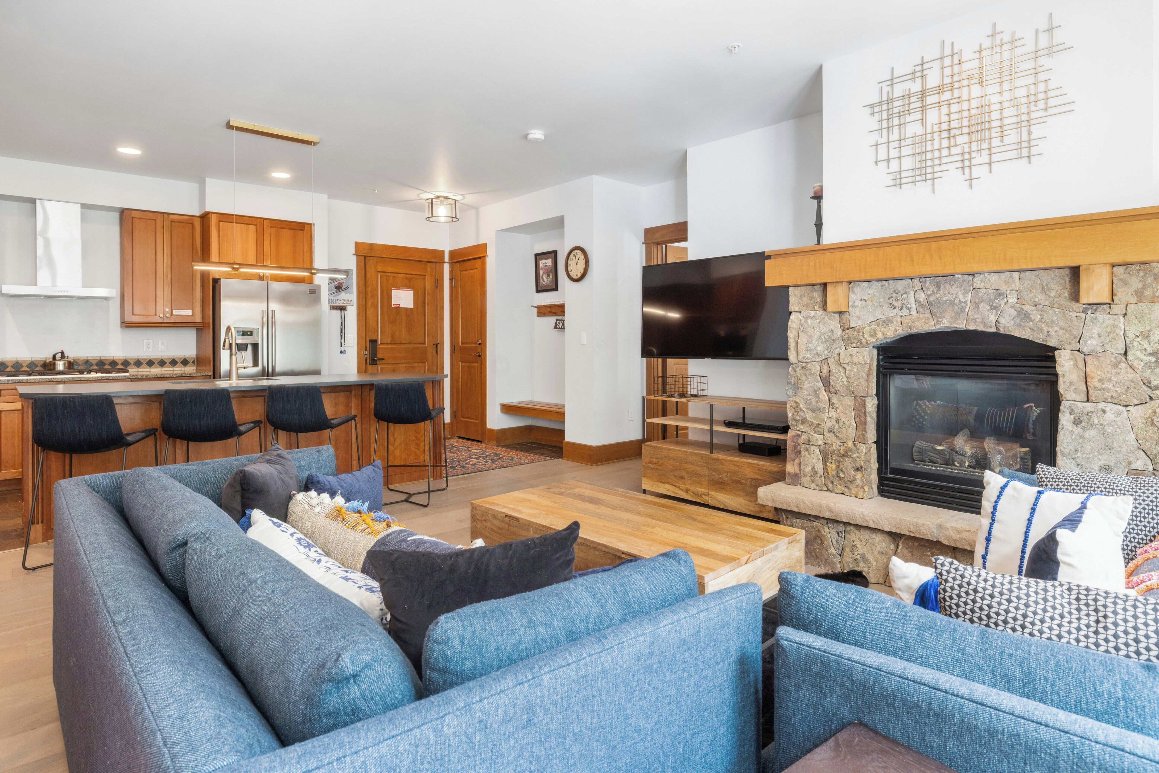 A modern living room with a blue sofa, a stone fireplace, and a kitchen in the background.