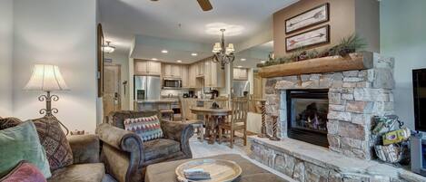 A spacious living room with a fireplace, a ceiling fan, and a kitchen in the background.