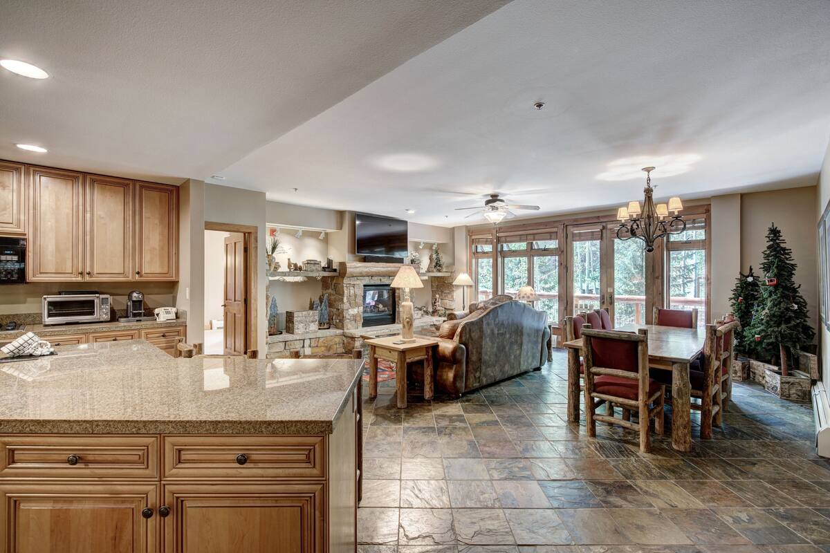 A spacious kitchen with granite countertops, wooden cabinets, and a stone floor.