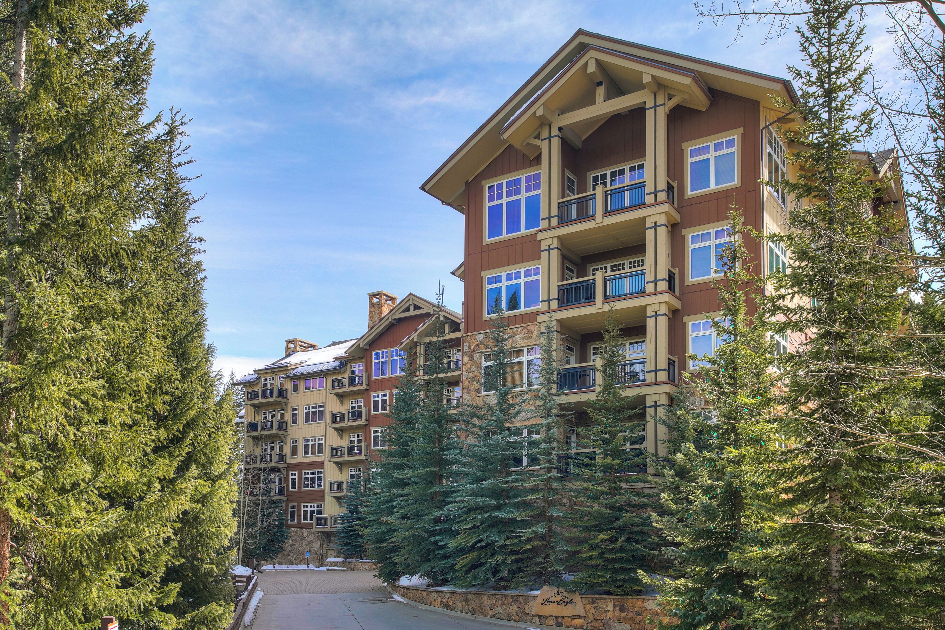 A multi-story hotel with balconies, surrounded by evergreen trees.