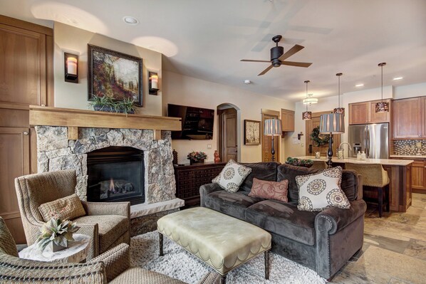 A spacious living room with a stone fireplace, comfortable seating, and a kitchen area with wooden cabinets and modern appliances.
