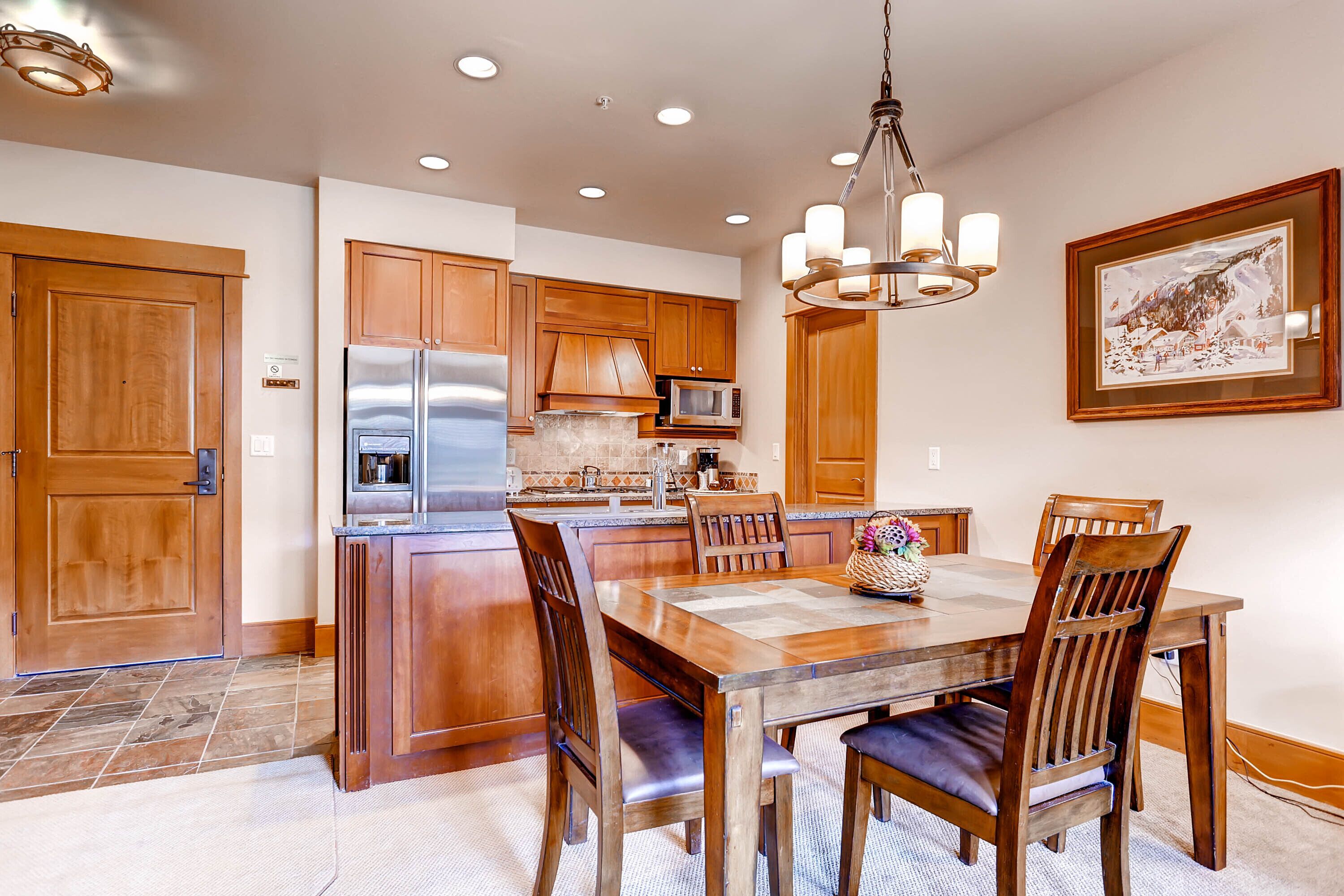 A kitchen with wooden cabinets, a stainless steel refrigerator, a microwave, and a chandelier.