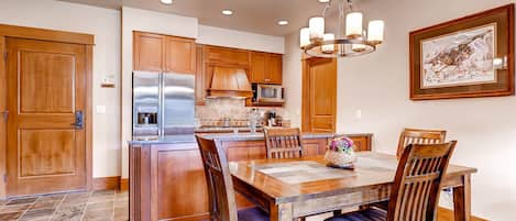 A kitchen with wooden cabinets, a stainless steel refrigerator, a microwave, and a chandelier.