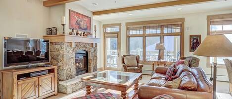 A cozy living room with a stone fireplace, leather sofa, and a television on a wooden cabinet.