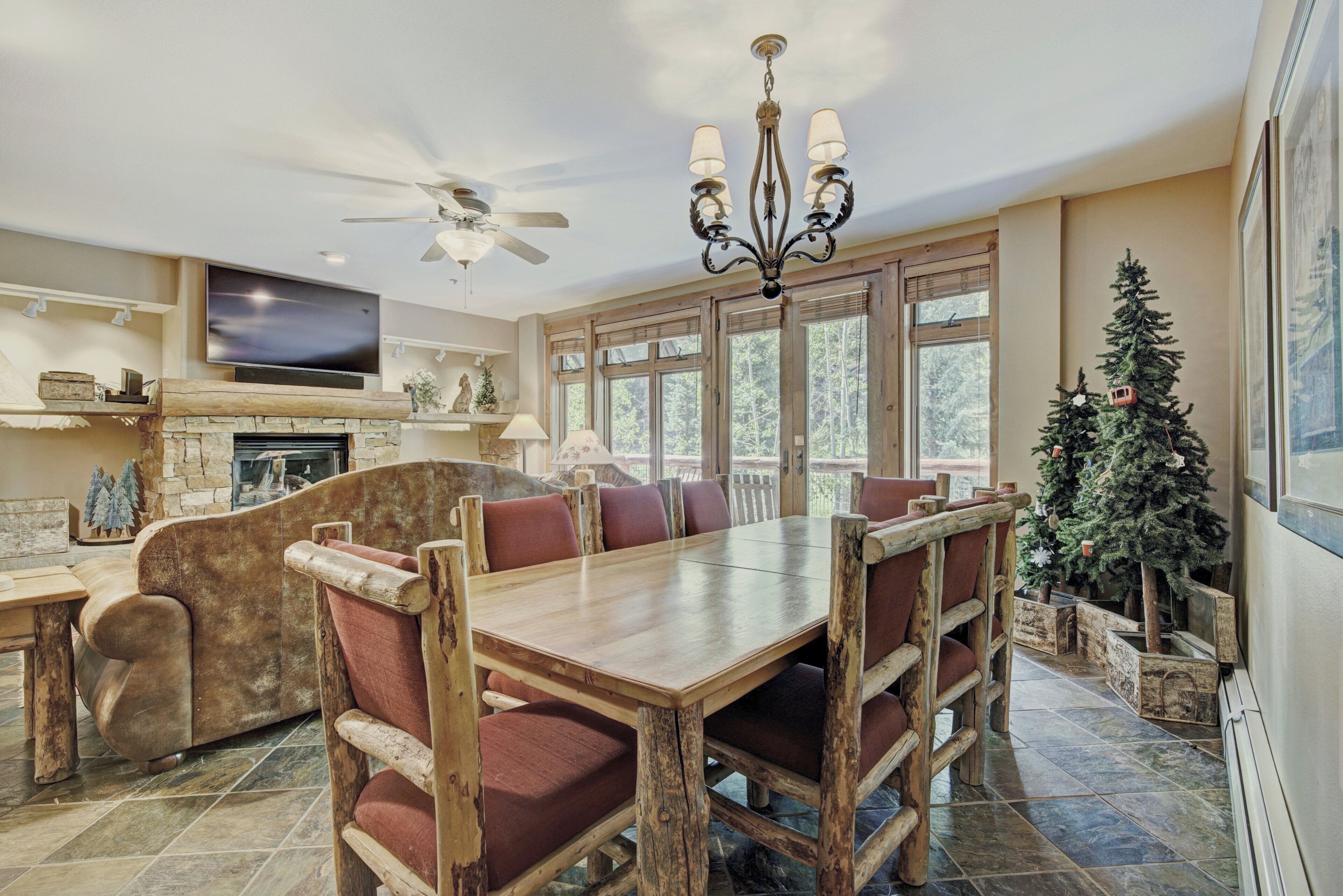 A spacious dining area with a wooden table and chairs, a fireplace, and a large window with a view of trees.