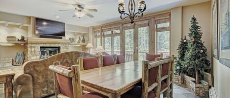 A spacious dining area with a wooden table and chairs, a fireplace, and a large window with a view of trees.