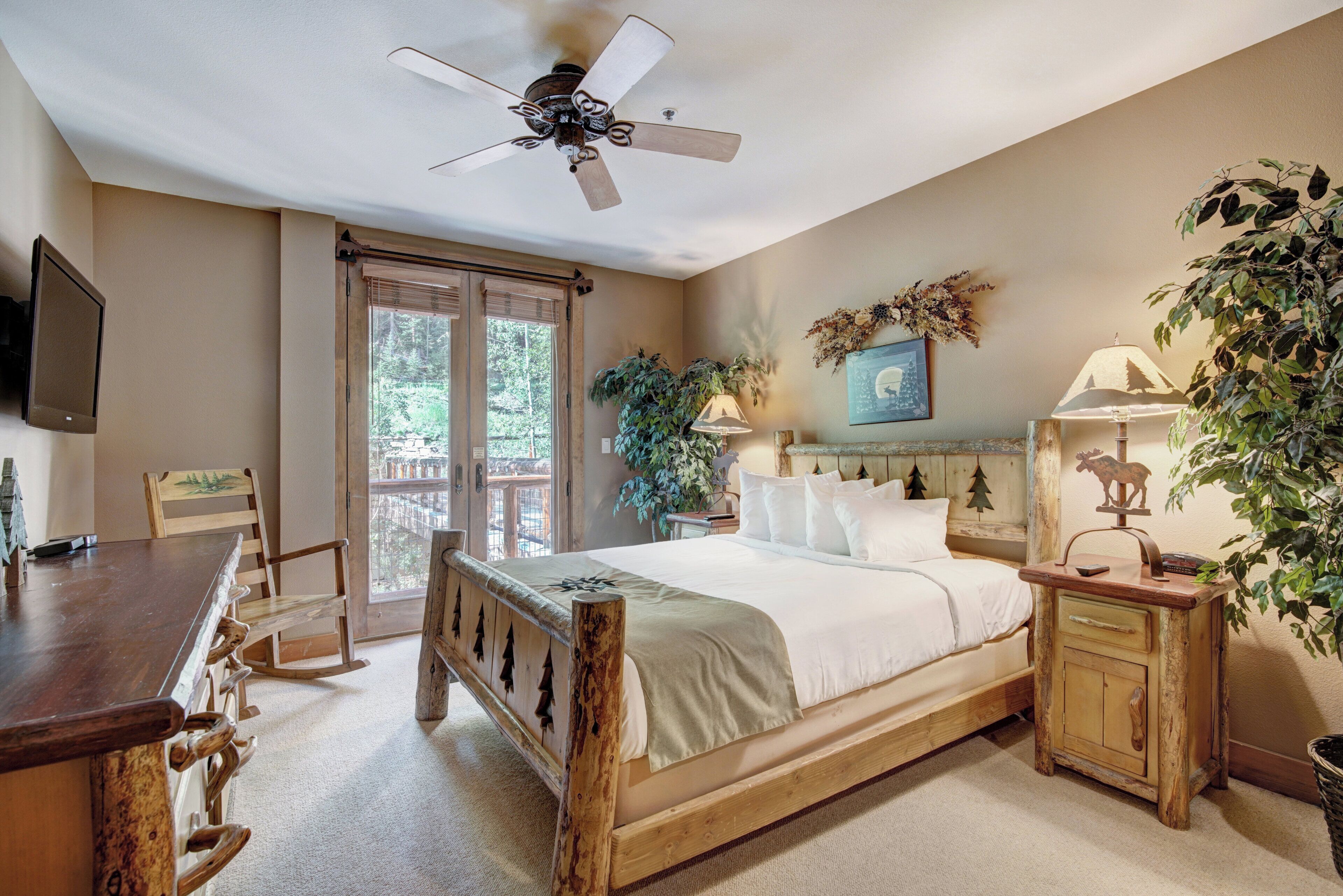 A bedroom with a wooden bed, a ceiling fan, a desk with a chair, and a window with blinds.