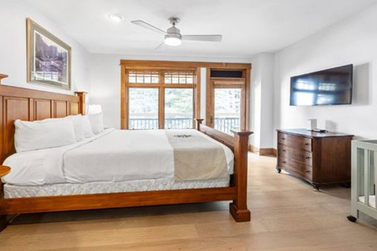 A bedroom with a wooden bed, a nightstand, a dresser, a TV, and a crib.