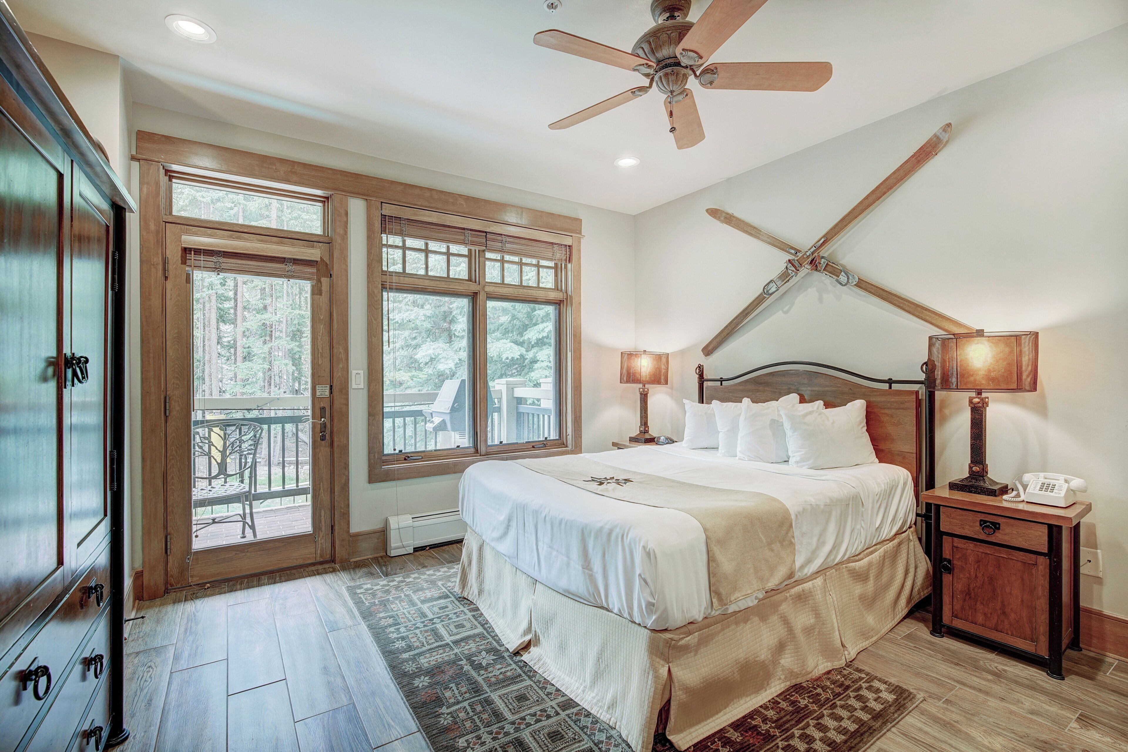 A bedroom with a large bed, two bedside tables with lamps, a ceiling fan, and a view of the outdoors through a sliding door.