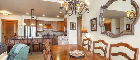 A spacious dining area with a wooden table and chairs, a chandelier, and a large mirror on the wall.