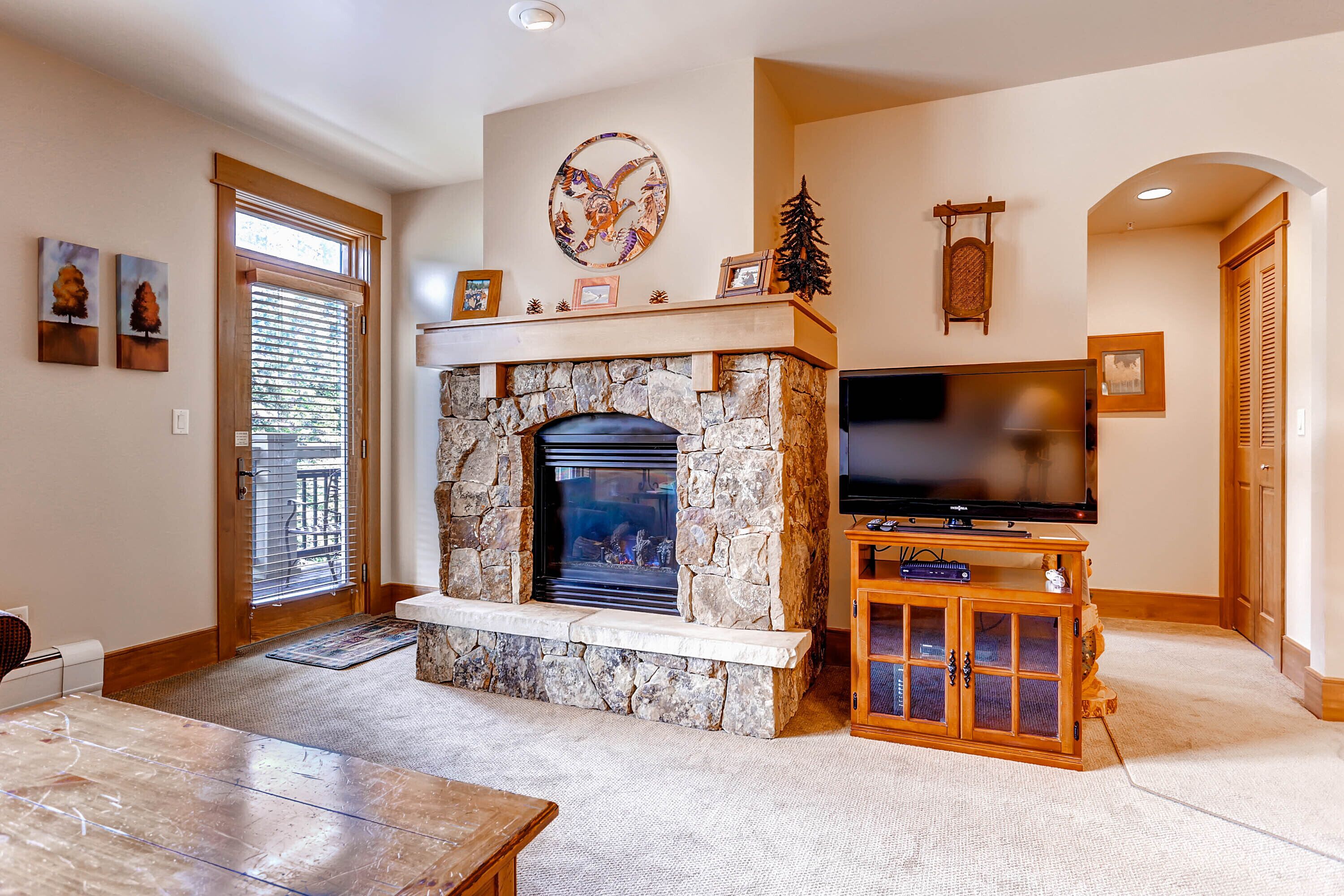 A living room with a stone fireplace, a television on a wooden stand, and a door with a glass panel.