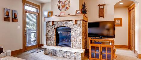 A living room with a stone fireplace, a television on a wooden stand, and a door with a glass panel.