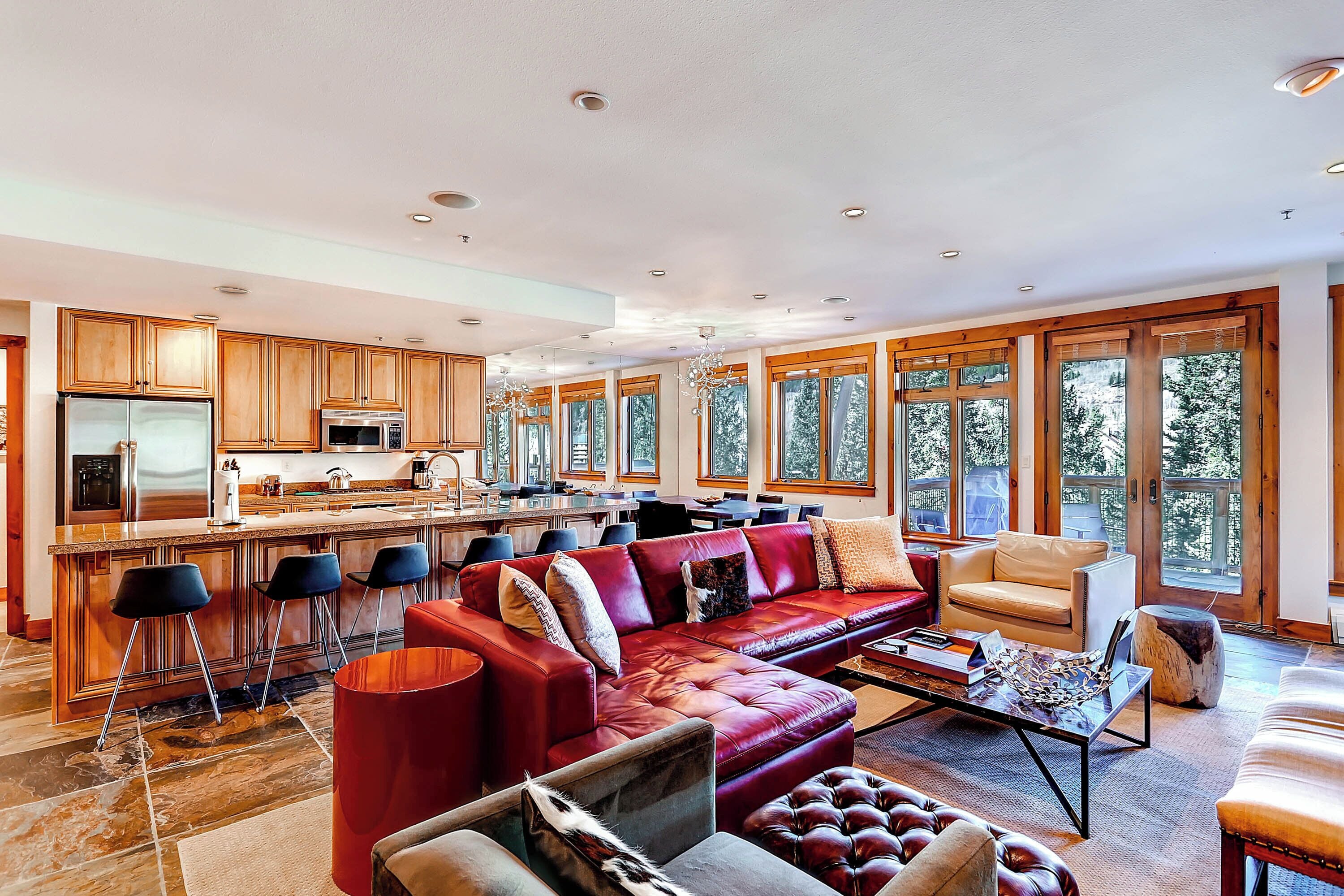 A spacious living area with a red leather sofa, a coffee table, and a large window offering a view of trees.