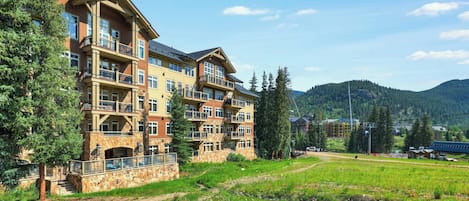 A multi-story hotel with balconies, stone facade, and a view of the surrounding forest and mountains.