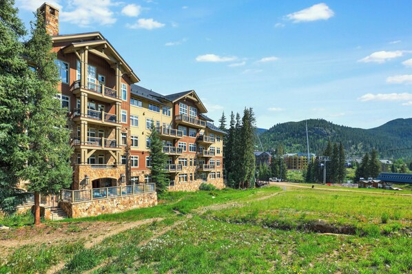 A multi-story hotel with balconies, stone facade, and a view of the surrounding forest and mountains.
