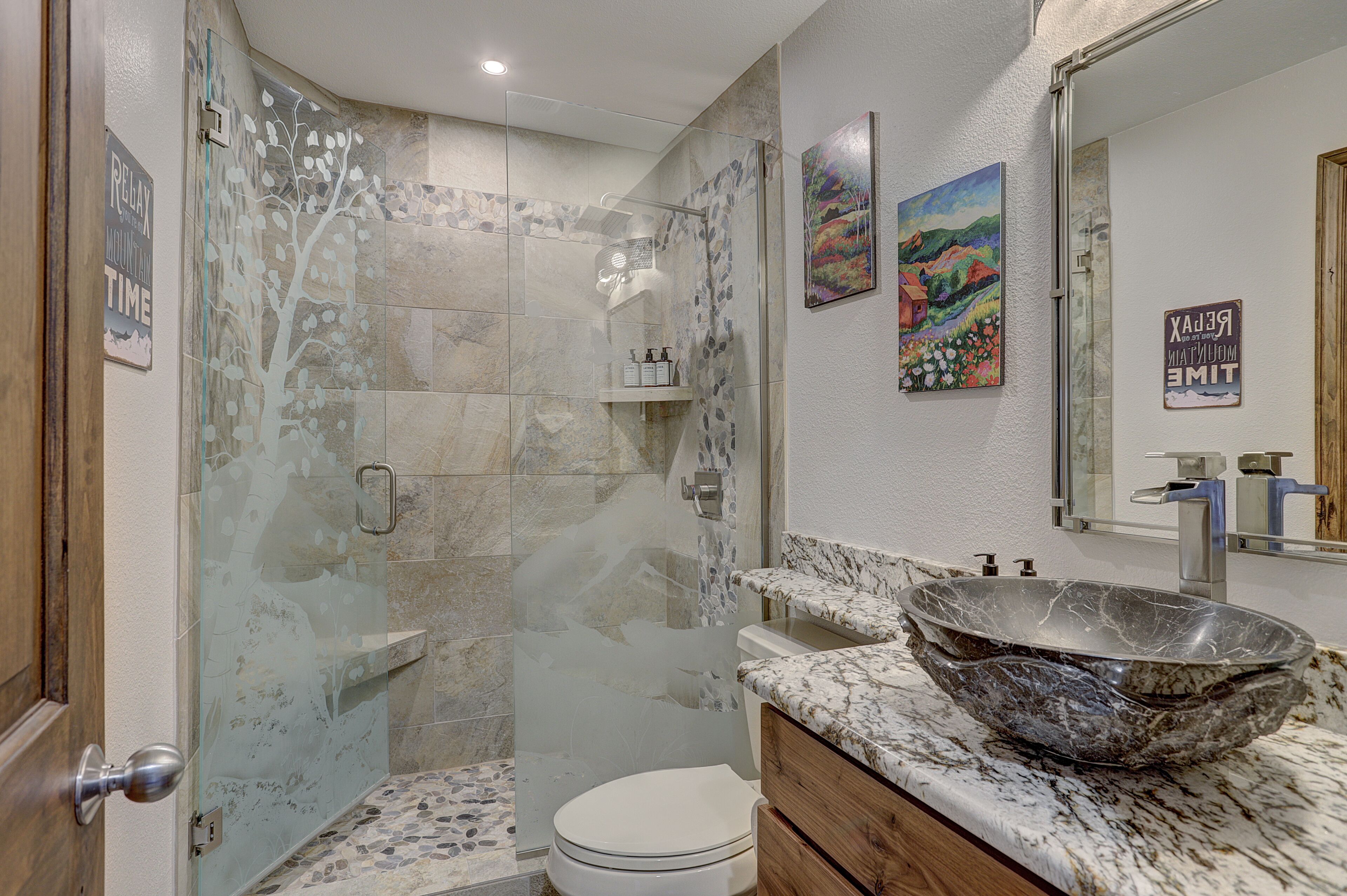 A bathroom with a glass-enclosed shower, a marble sink, and a toilet.