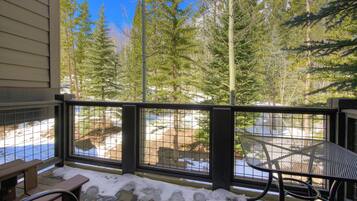 A wooden deck with a metal table and benches, overlooking a snowy landscape and dense forest.