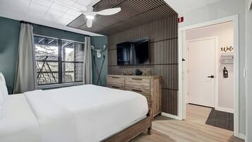 A bedroom with a large bed, a TV mounted on the wall, a wooden dresser, and a ceiling fan.