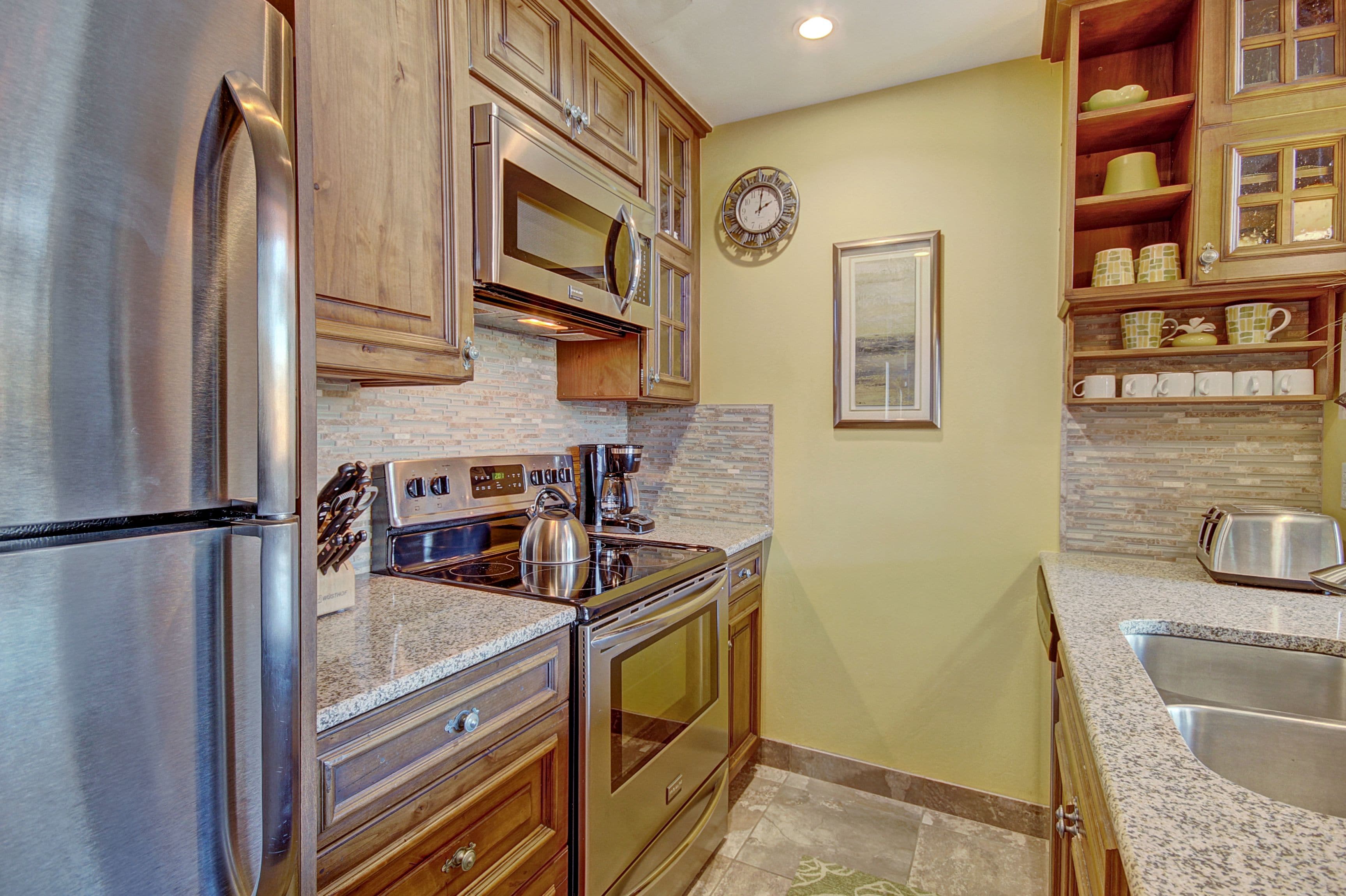 A kitchen with stainless steel appliances, wooden cabinets, a granite countertop, and a backsplash.