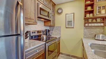 A kitchen with stainless steel appliances, wooden cabinets, a granite countertop, and a backsplash.