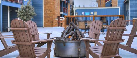 A snow-covered outdoor seating area with Adirondack chairs around a metal fire pit.