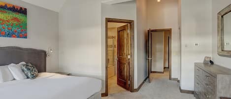 A bedroom with a large bed, a dresser, and a door leading to another room.