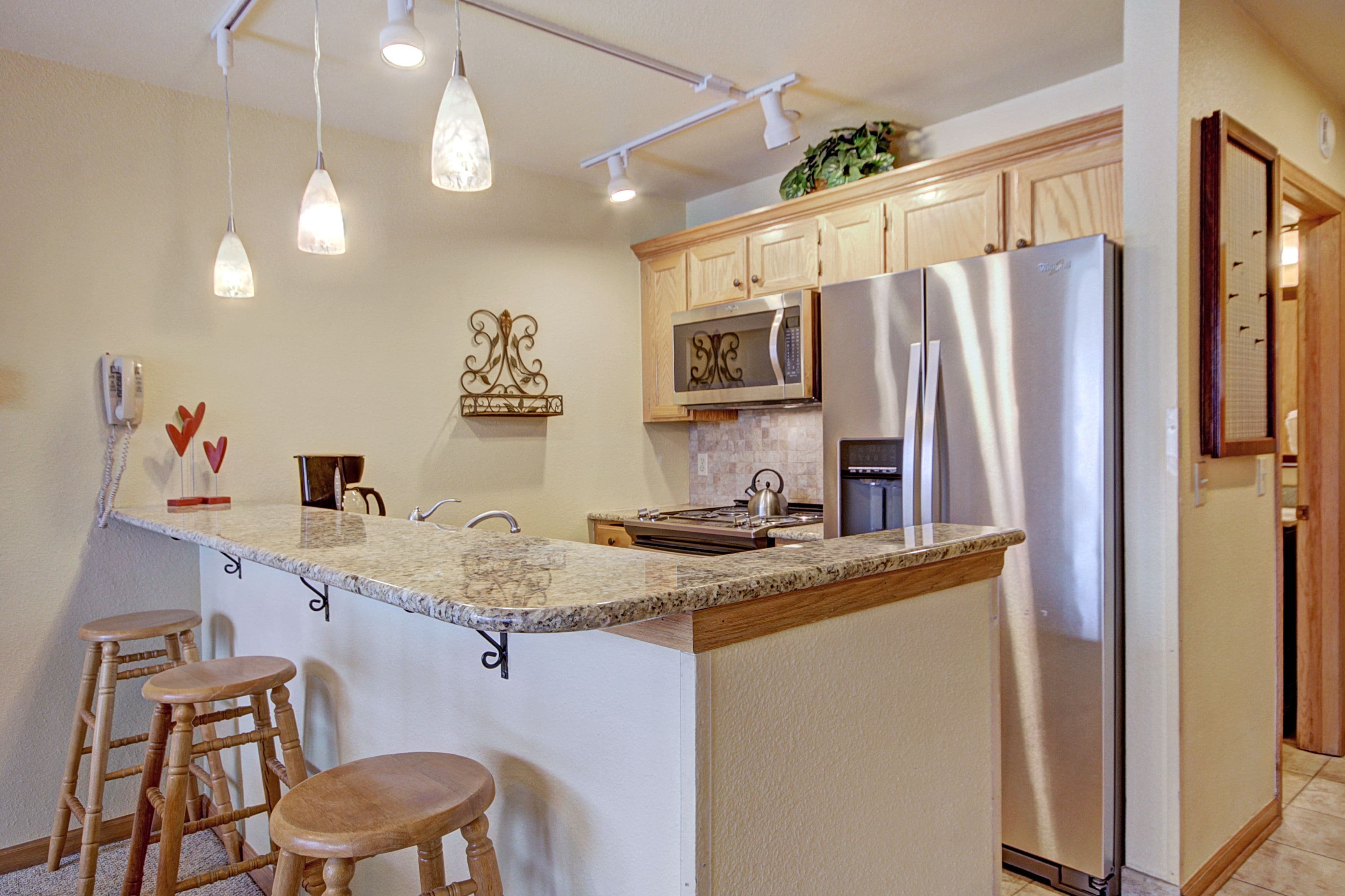 A kitchen with a central island, bar stools, stainless steel appliances, and pendant lighting.