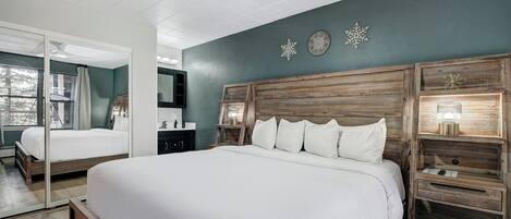 A bedroom with a large bed, a wooden headboard, a nightstand with a lamp, and a mirror.