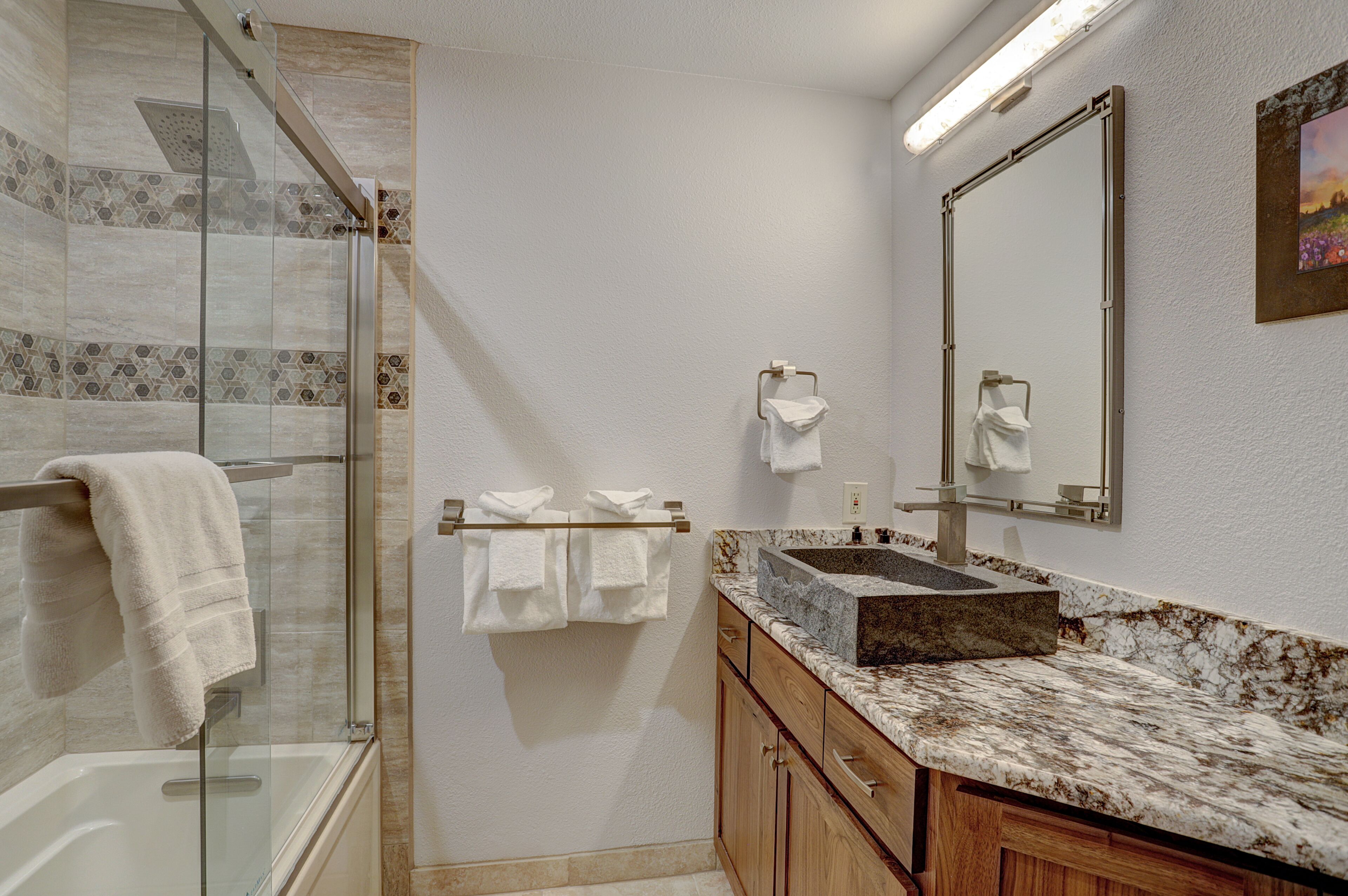 Une salle de bain moderne avec une douche à parois de verre, un lavabo en marbre, des meubles en bois et un grand miroir.